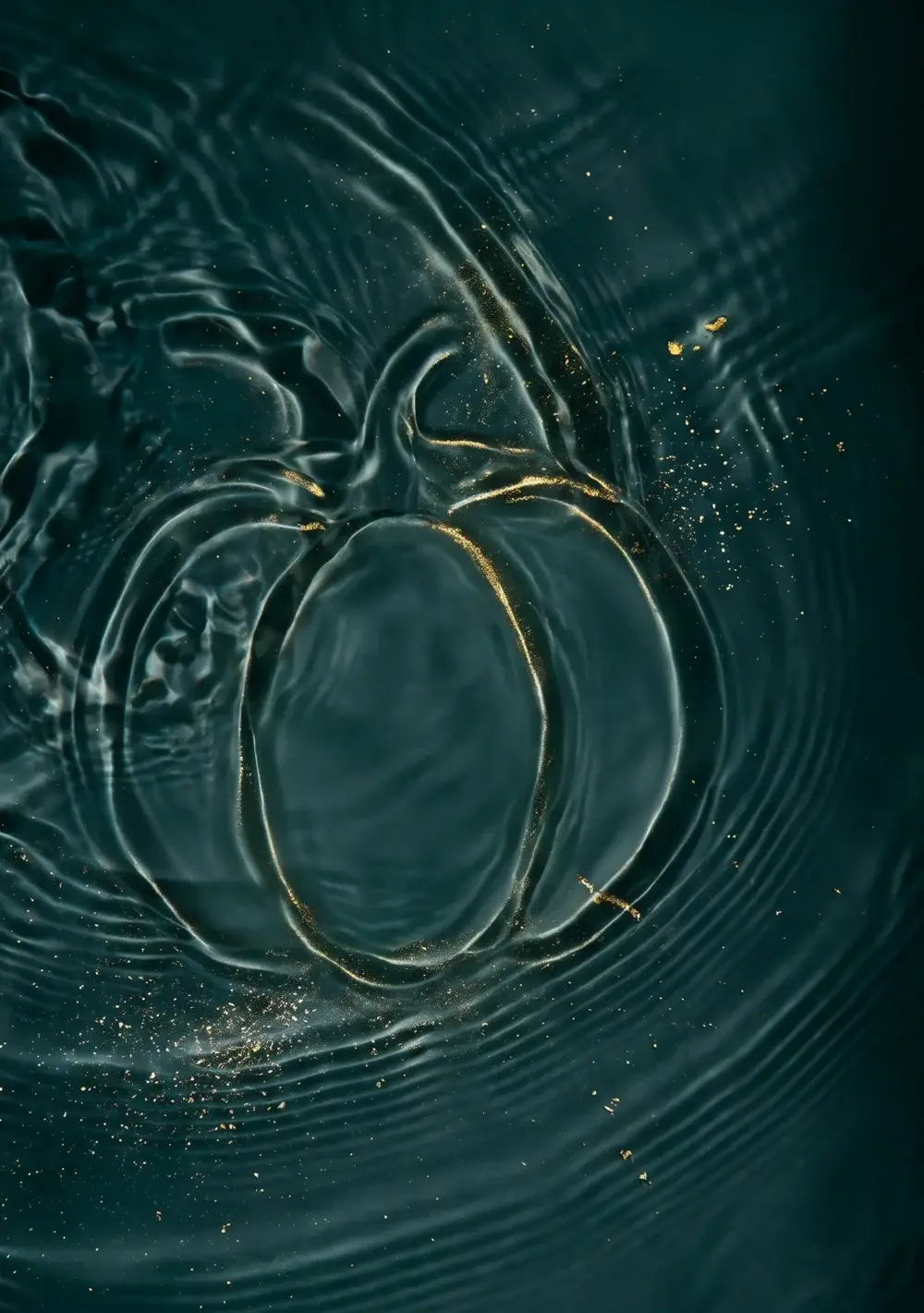A pumpkin shape traced in gold-flecked ripples on dark teal water, for the Well Labs Dallas Boo-Tox Party