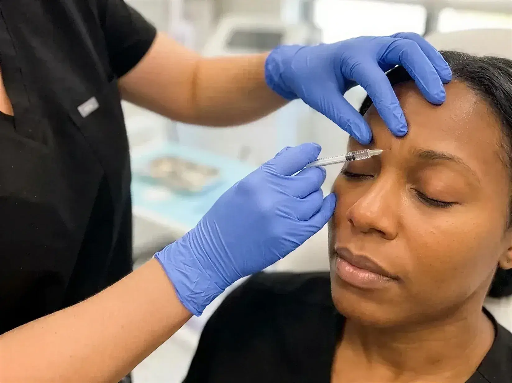 A gloved provider administering a Daxxify injection between a client's brows