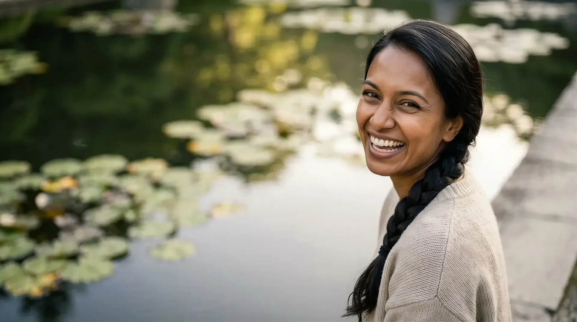 Smiling woman with a fresh, healthy complexion beside a garden pond in warm light, evoking a customized facial plan in Dallas