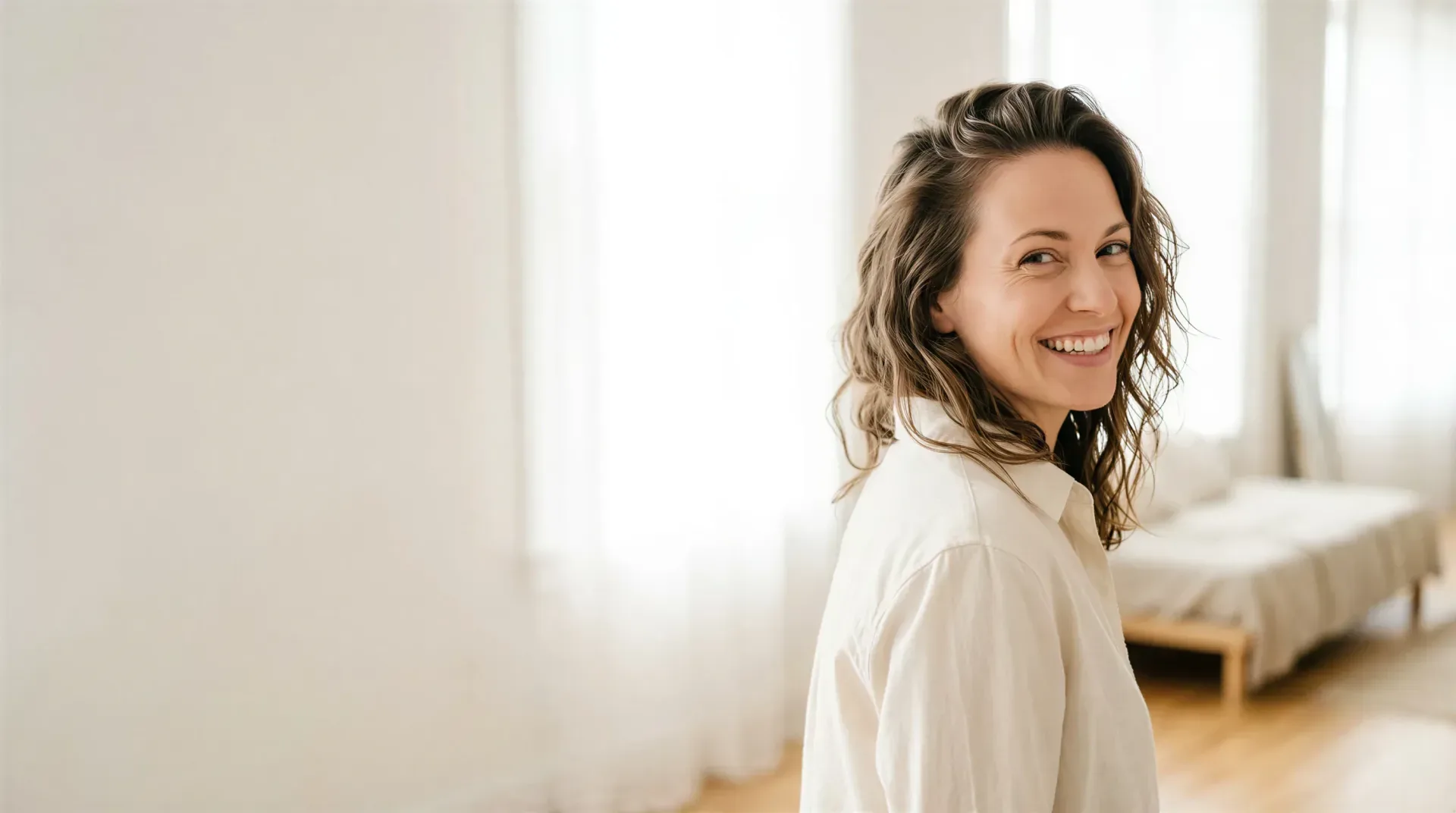 Smiling woman with clear, even skin in a bright, airy room, evoking IPL photofacial results that fade sun damage in Dallas