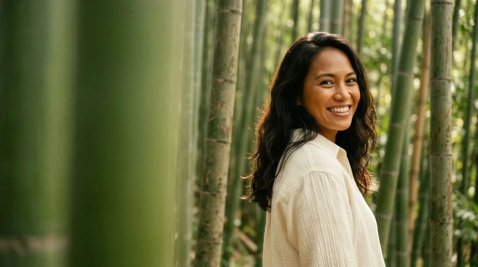 Smiling woman in a sunlit bamboo forest, evoking natural-looking Juvéderm filler results from a Dallas medical spa