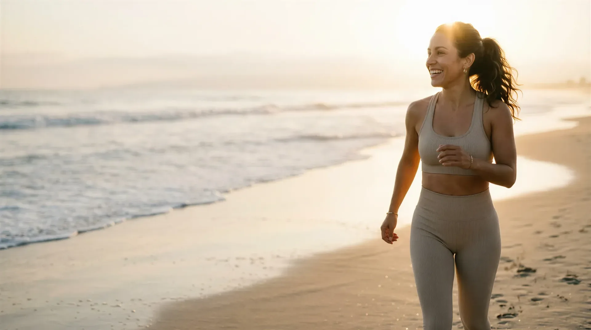 Smiling woman jogging on a sunlit beach at golden hour, evoking non-surgical body toning and shaping in Dallas