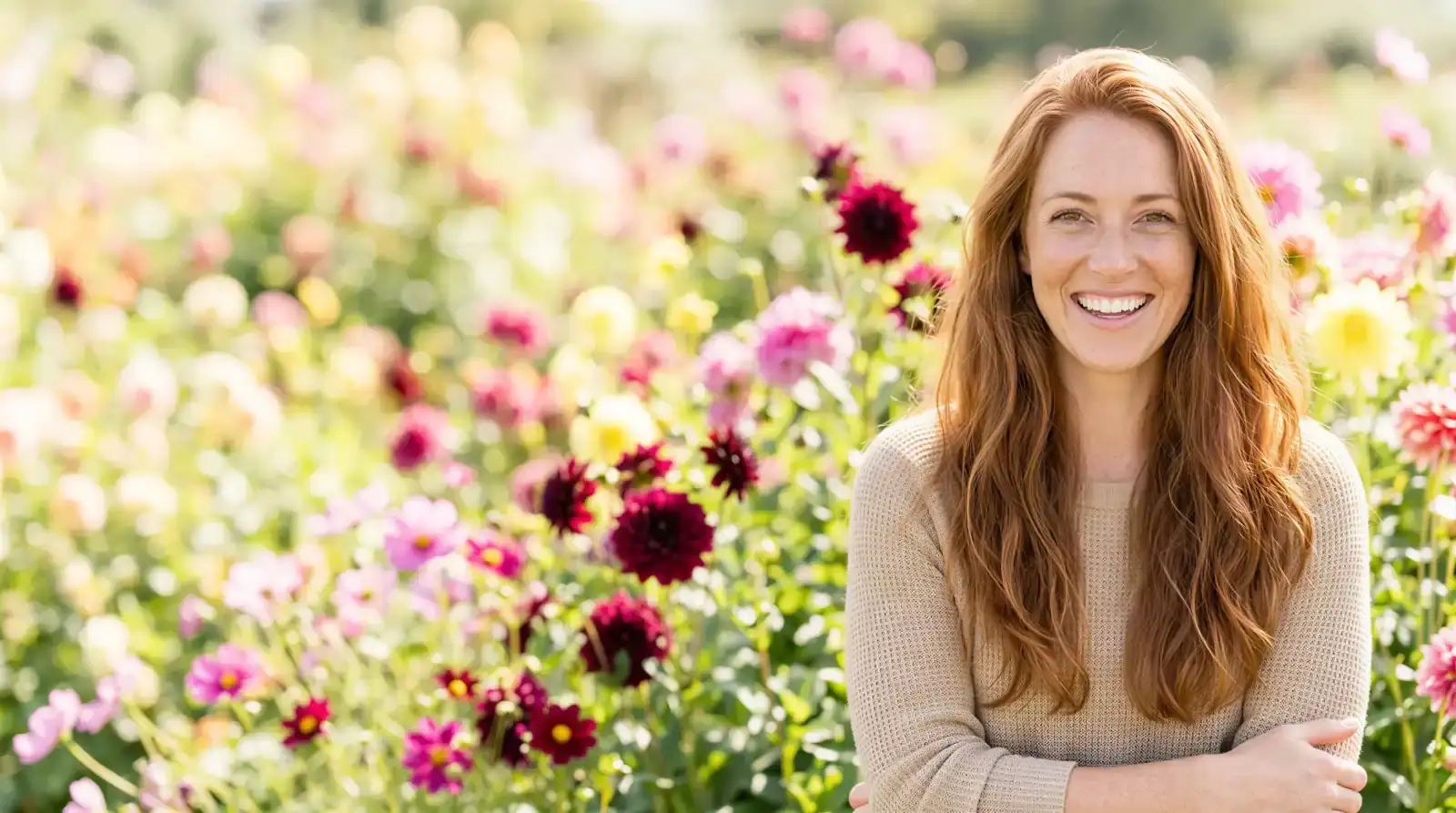 Smiling red-haired woman with folded arms in a sunlit Dallas flower garden