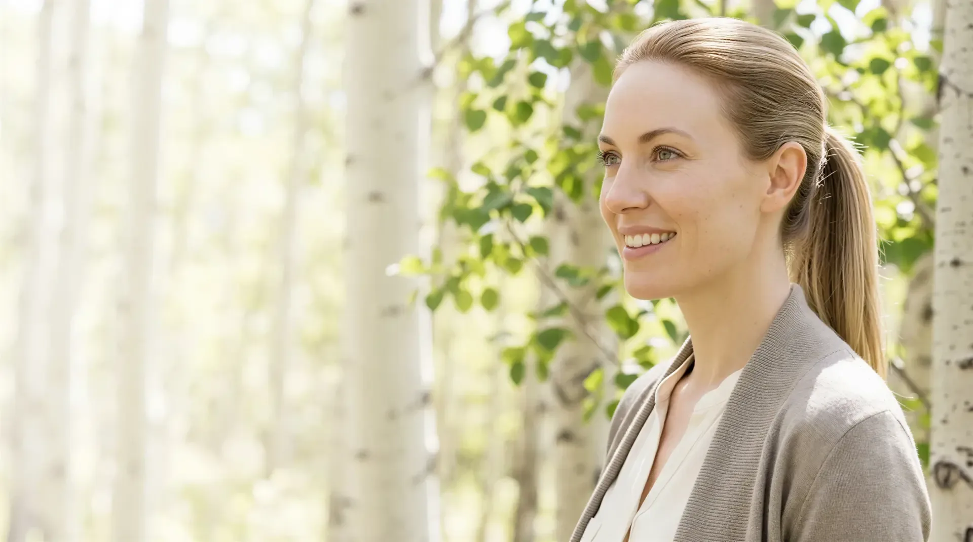 Woman smiling in profile among sunlit aspen trees, looking calm and well