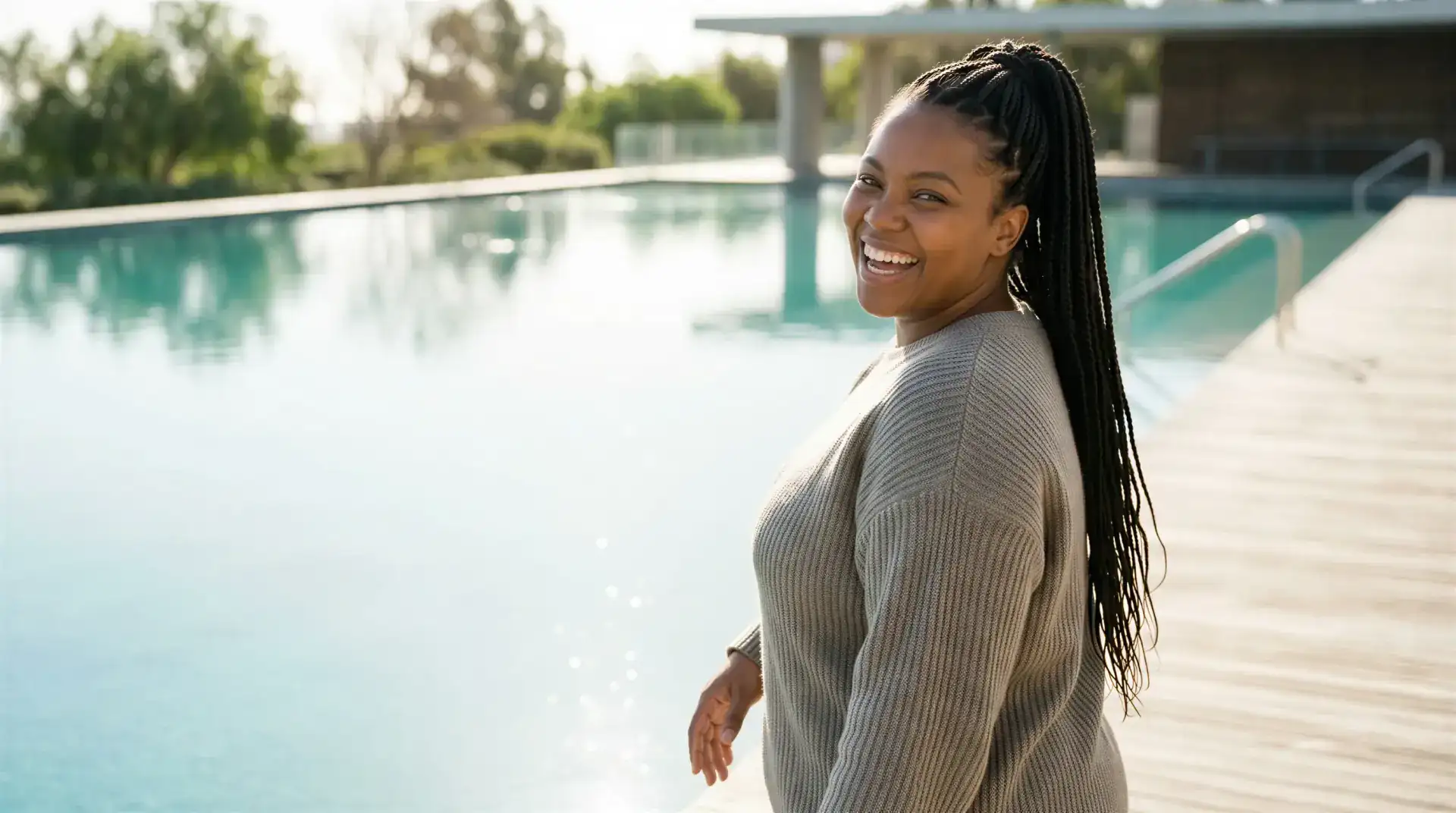 Smiling woman with long braids standing beside a sunlit infinity pool in Dallas, evoking the skin and hair renewal of PRF injections