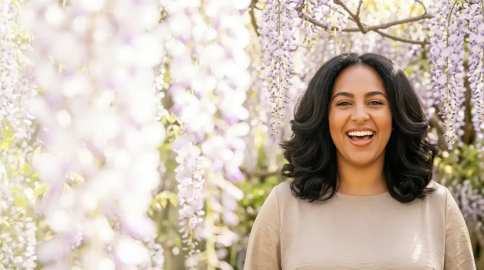 Smiling woman with bright, even-toned skin among blooming wisteria in soft daylight, evoking clearer skin tone and texture after a VI Peel in Dallas