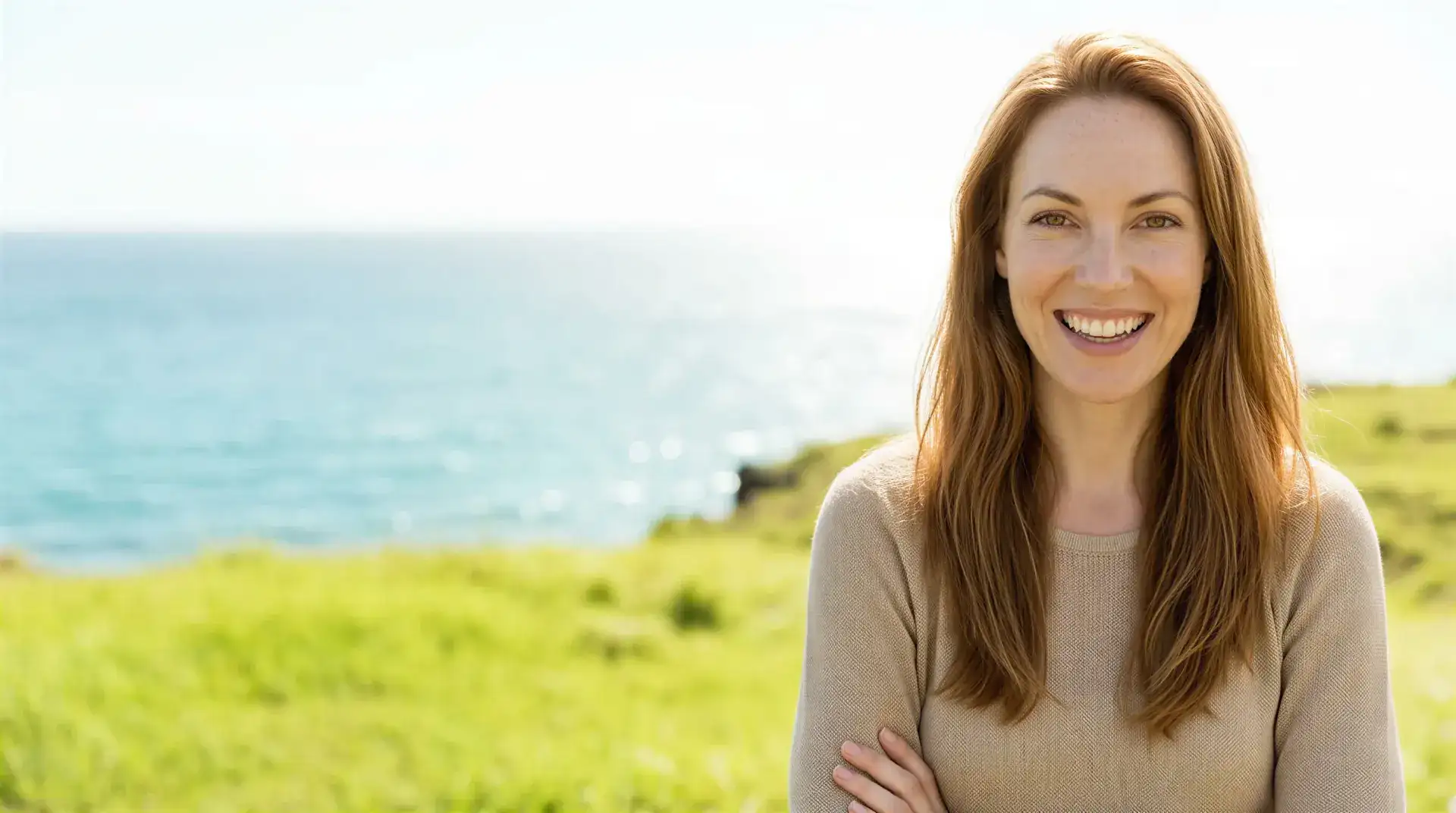 Smiling woman with auburn hair outdoors by the ocean in warm sunlight, evoking smoother skin after zWave cellulite treatment in Dallas