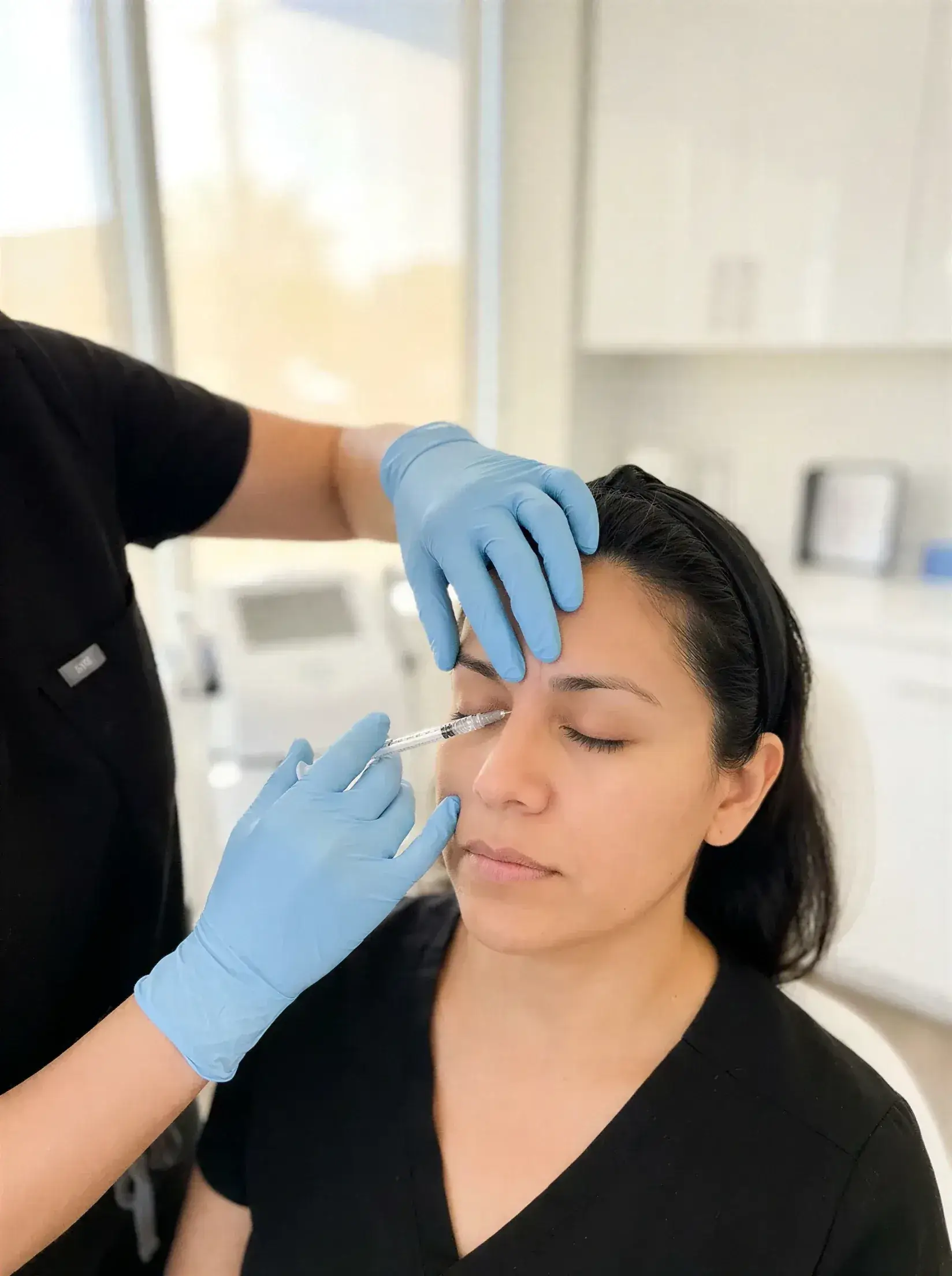 A gloved provider administering a Jeuveau injection to smooth the frown lines between a client's brows