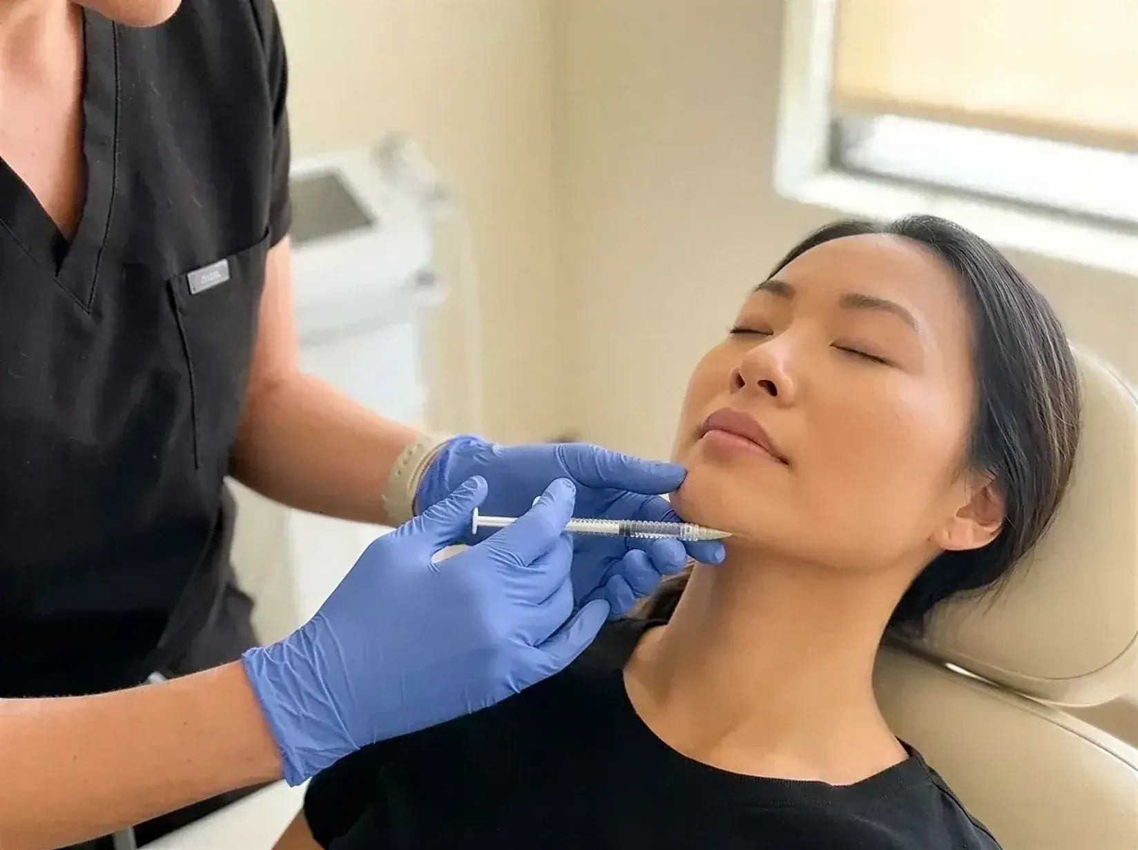 A gloved provider administering a masseter Botox injection along a client's jawline