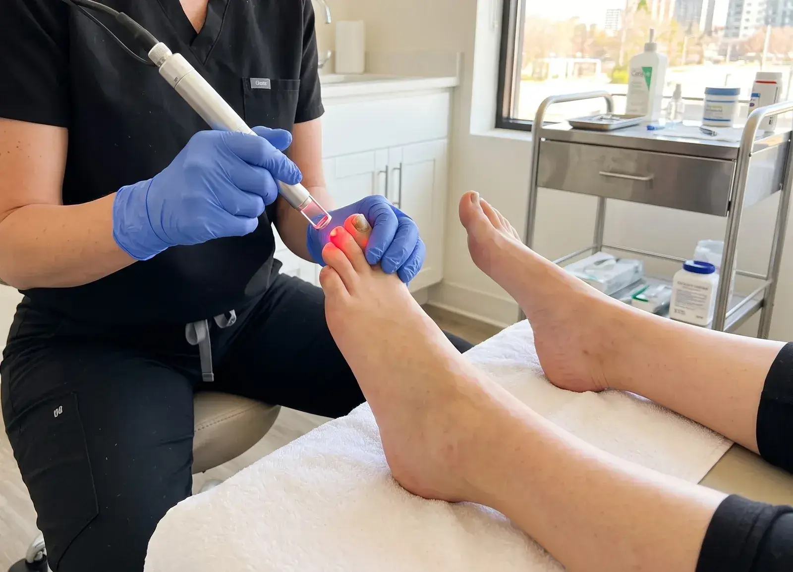 A gloved Well Labs+ provider directing a handheld laser at a client’s toe during an in-office laser nail-fungus treatment