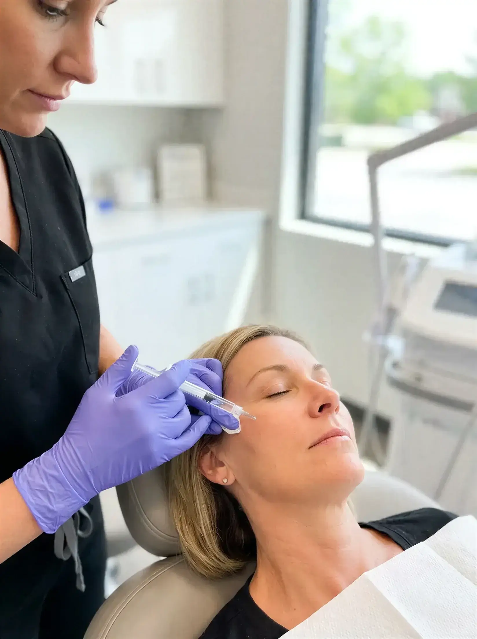 A gloved provider injecting Restylane dermal filler into a client's cheek for mid-face volume