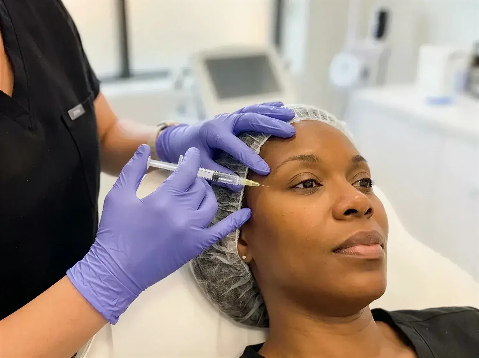 A gloved provider injecting Sculptra collagen-stimulating filler into a client's upper cheek